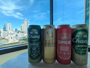 チャオプラヤー川と高層ビルを背景に並んだタイのビール缶